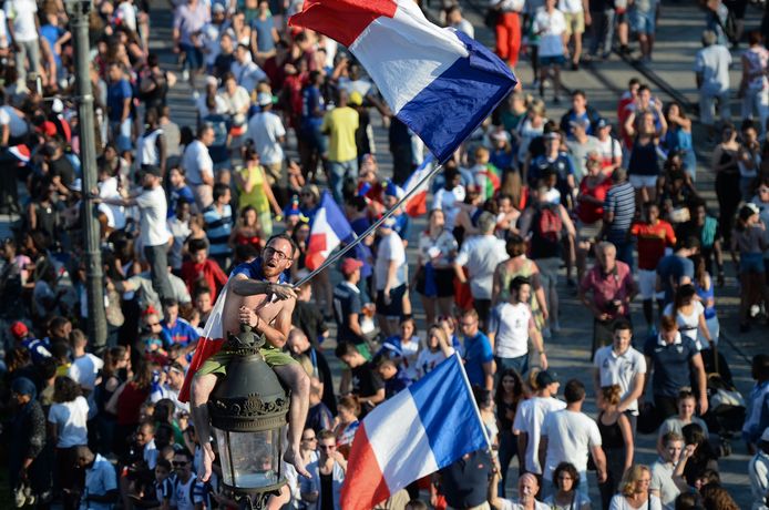 Een Franse fan klimt met de nationale driekleur in een lantaarnpaal.