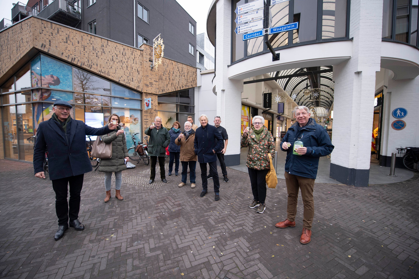 Blije bestuursleden van ondernemersvereniging CAA toasten bij de ingang van de Galerij op de BIZ. Met rechts vooraan  voorzitter Ben Kamp en links wethouder Jan Martin van Rees.