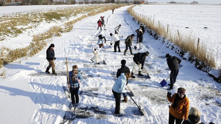 Tientallen vrijwilligers maken het ijs op de route van de Elfstedentocht bij Hindeloopen sneeuwvrij. © ANP Beeld 