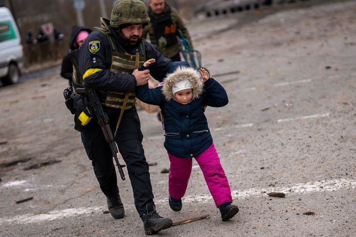 A Ukrainian police officer runs while holding a child as the artillery echoes nearby, while fleeing Irpin on the outskirts of Kyiv, Ukraine, Monday, March 7, 2022. (AP Photo/Emilio Morenatti)