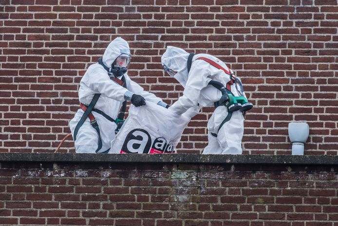 Twee werklieden verwijderen asbest, gehuld in beschermende pakken