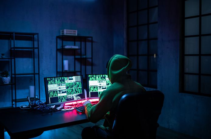 Hacker man working on computers alone in dark room, rear view.