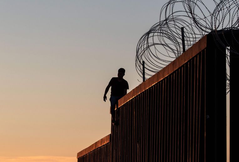 Een man op de muur die op de grens tussen Mexico en de Verenigde Staten staat.  Beeld AFP