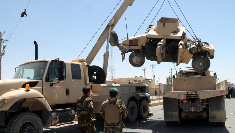 Afghaanse soldaten kijken woensdag toe hoe een militair voertuig wordt weggehaald, dat werd beschadigd bij een aanslag in de provincie Helmand, waarbij tien doden vielen. Beeld epa