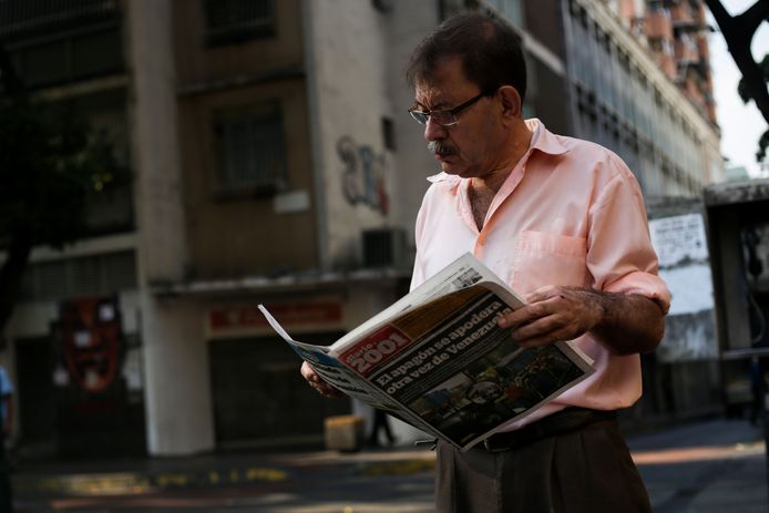 Een Venezolaanse man leest de krant. ‘Stroomstoring heeft Venezuela opnieuw in zijn greep’, luidt de kop.