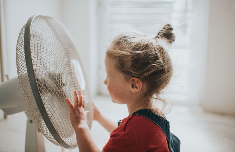 Little girl enjoying cooling experience of sitting by a large electric fan. Beeld Getty Images