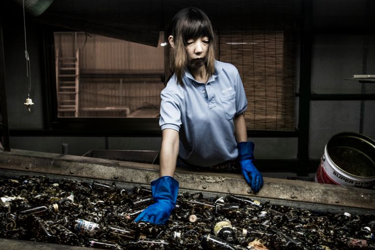 In Ryugasaki, Japan, wordt dagelijks 350 ton glas gerecycled. Kaori Kimchi (48) werkt sinds 2001 in de fabriek. Haar taak is het verwijderen van de rommel tussen de glazen flessen.  Beeld Kadir van Lohuizen