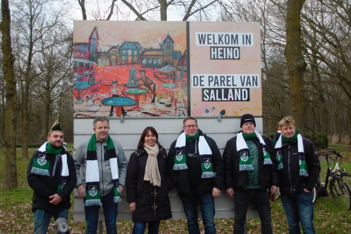 Vriendengroep de Oelewappers poseert trots voor het nieuwe welkomstbord in Heino dat zaterdag is onthuld.