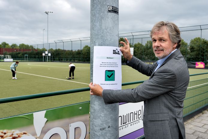 Voorzitter Jos korsten van hockeyclub De Hopbel plakt een coronacheckposter.