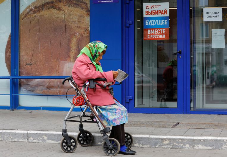 Een vrouw leest in Zaporizja een krant voor een winkel. Op de poster staat: ‘Kies een toekomst samen met Rusland.  Beeld REUTERS
