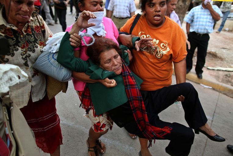 Een vrouw, flauwgevallen tijdens de bestorming van een mortuarium in Honduras, wordt weggedragen. Beeld ap