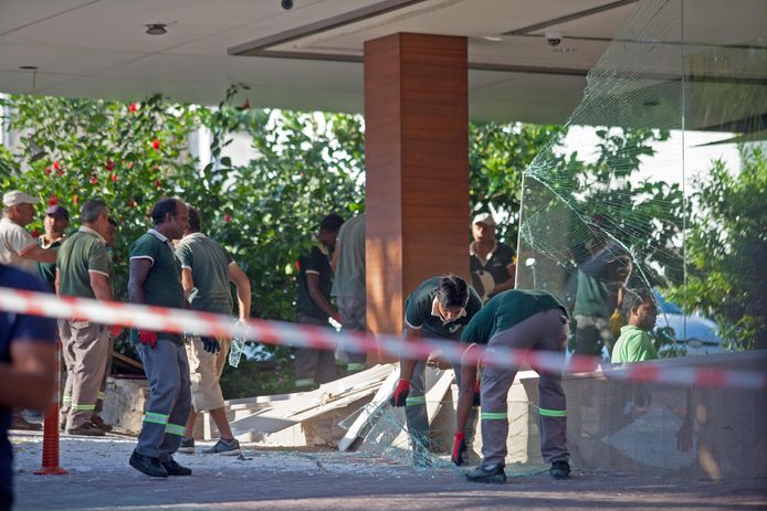 Werklieden ruimen het gebroken glas en puin op bij de ingang van het hotel.