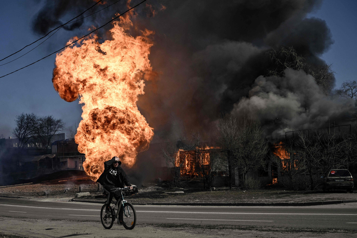 Een man fietst langs een brand die is ontstaan door artillerievuur in de stad Charkov.  Beeld Aris Messinis/AFP