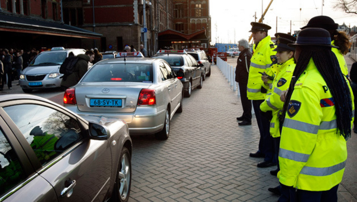 Politieagenten houden een oogje in het zeil tijdens de opening van de vernieuwe taxistandplaats aan het Amsterdamse Centraal Station in 2008. Vanaf dat moment konden alleen nog kwaliteitstaxi's met een belanghebbendenvergunning op de taxistandplaats Centraal Station hun diensten aanbieden. Op die manier wilde de gemeente ervoor zorgen dat het taxiaanbod weer een visitekaartje voor de stad wordt. Desondanks blijft het behelpen met de kwaliteit Amsterdamse taxi's. © anp Beeld 