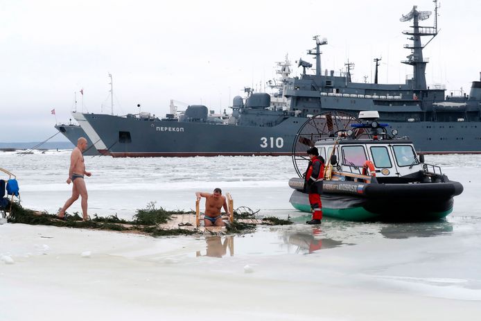 Enkele Russen nemen een ijsberen-duik in het water bij het Russische Kronstadt, met een oorlogsschip in de achtergrond. Beeld van gisteren.