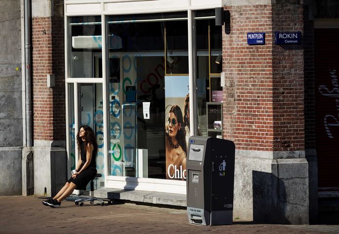 Een medewerkster van een winkel geniet van de zon op het Muntplein.