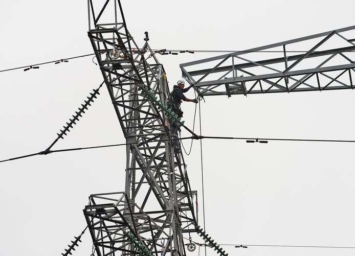 Twee mannen van installatiebedrijf Spie bovenop een van de oude elektriciteitsmasten, waar ze de nieuwe mast begeleiden naar de nieuwe voet.