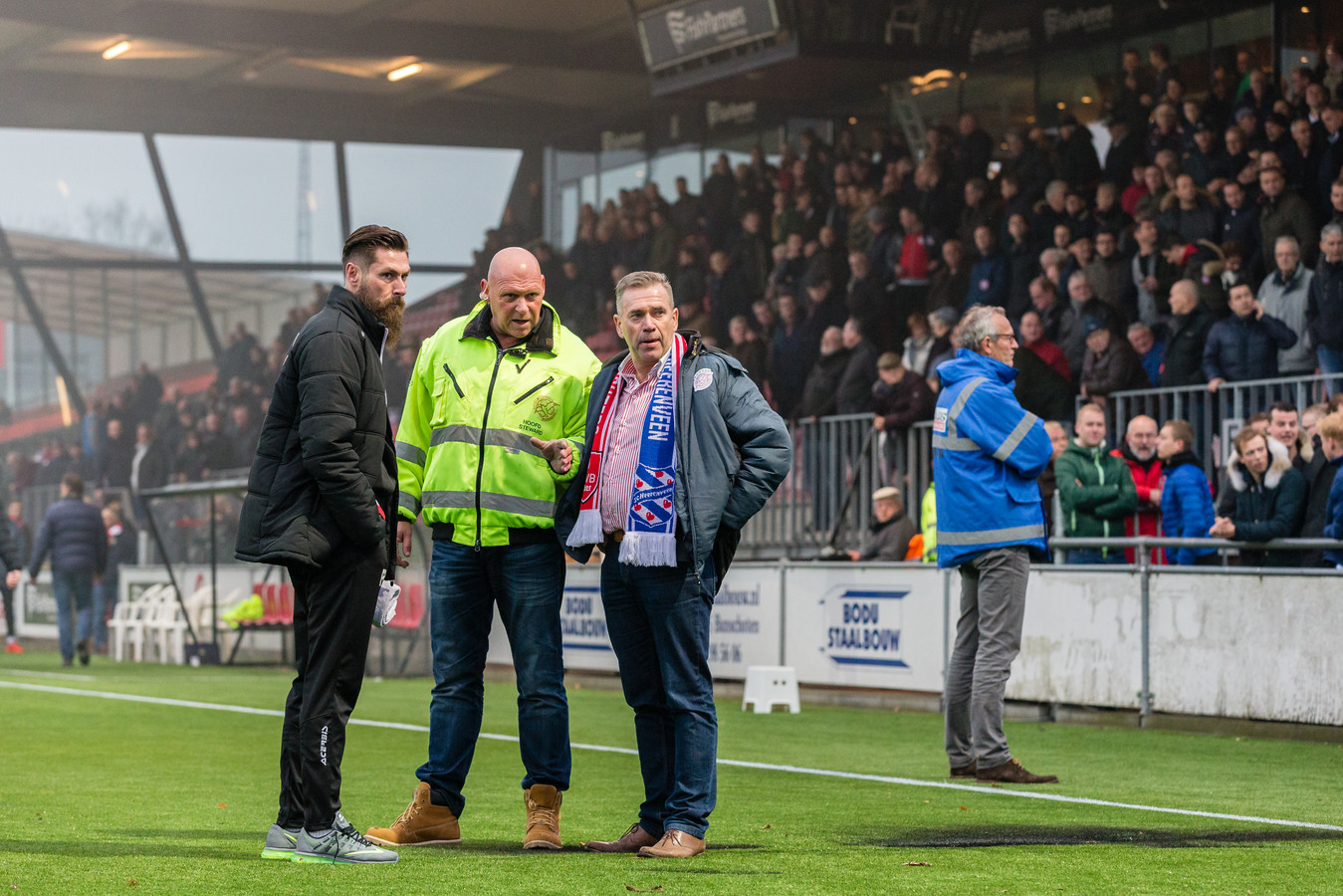 Voorzitter Frank van den Bos inspecteert het veld met Pascal Bosschaart en een steward, rechts achter de schroeiplek houdt een steward van Quick Boys de aanhang van die club in de gaten.
