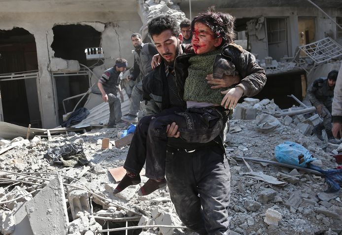 Een man redt een gewond kind uit een gebombardeerd gebouw in Hamouria, Oost-Ghouta.