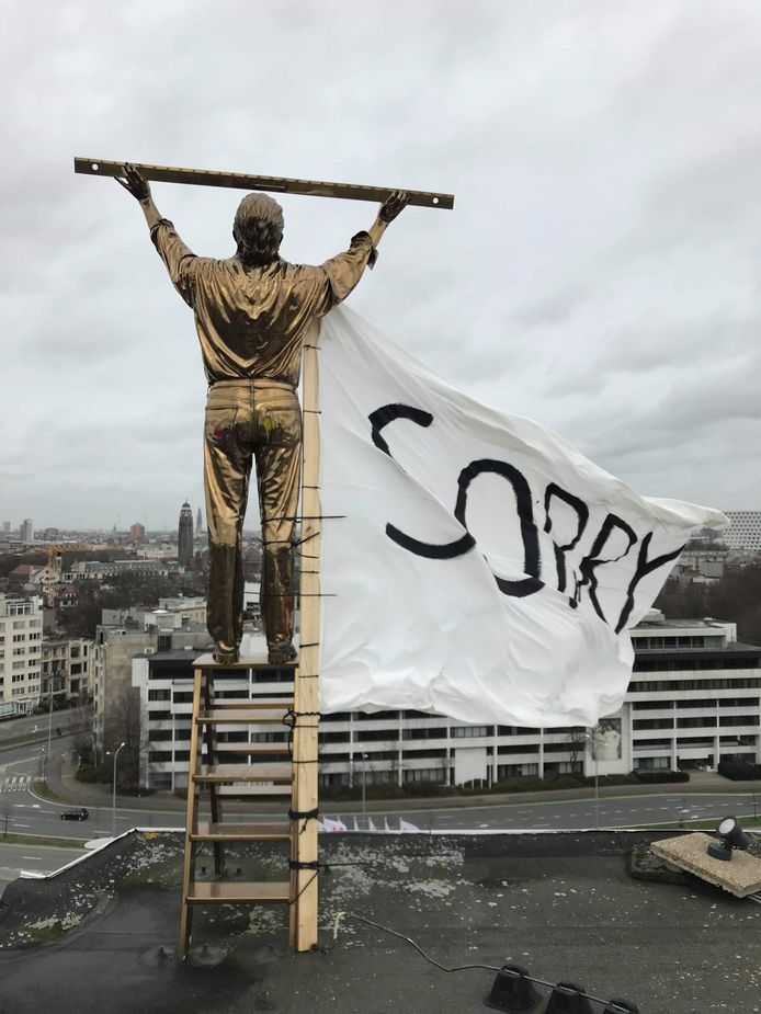 Een spandoek met de boodschap 'Sorry' wordt aan Fabres kunstwerk 'De man die de wolken meet' gehangen.