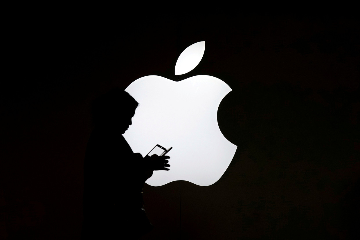Een vrouw kijkt op haar telefoon voor het logo van een Apple-winkel in Sjanghai, China.  Beeld Reuters