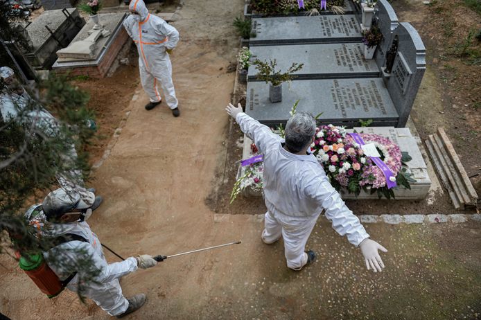 Een begrafenisondernemer gehuld in een beschermend pak wordt ontsmet door de stadsmedewerkers.