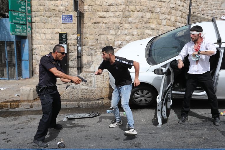 Een Israëlische politieagent (L) richt zijn pistool op een Palestijnse man (M) naast een gewonde Joodse man (R) in Jeruzalem. Beeld EPA