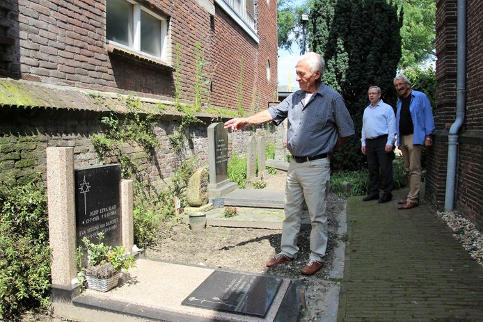 Cees van Schie, beheerder van de kerk, wijst op het bijzondere detail: een katholiek en Joods teken op de grafsteen. Predikant Zijlstra en scriba Metselaar luisteren naar zijn uitleg.
