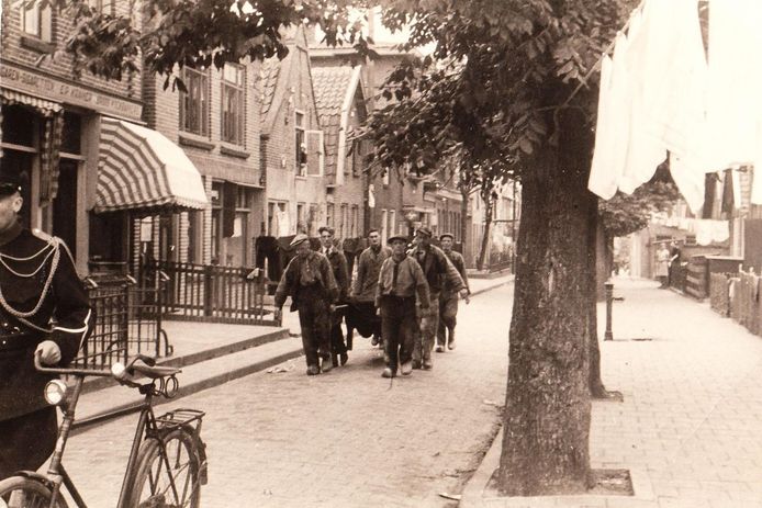 Gemeentearbeiders dragen op Urk de kist met het stoffelijk overschot van een geallieerde vlieger naar de haven. Het IJsselmeer was een belangrijke vliegroute voor geallieerde vliegtuigen die in Duitsland bombardementen uitvoeren. Veel omgekomen piloten spoelden op Urk aan. De man met de fiets aan de hand is mogelijk opperwachtmeester van de politie Harmen Visser. Hij was tot 1943 hoofd van de politie van Urk en actief in het verzet. Op 16 april 1945, één dag voor de bevrijding van de polder, sneuvelde hij bij Kuinre.