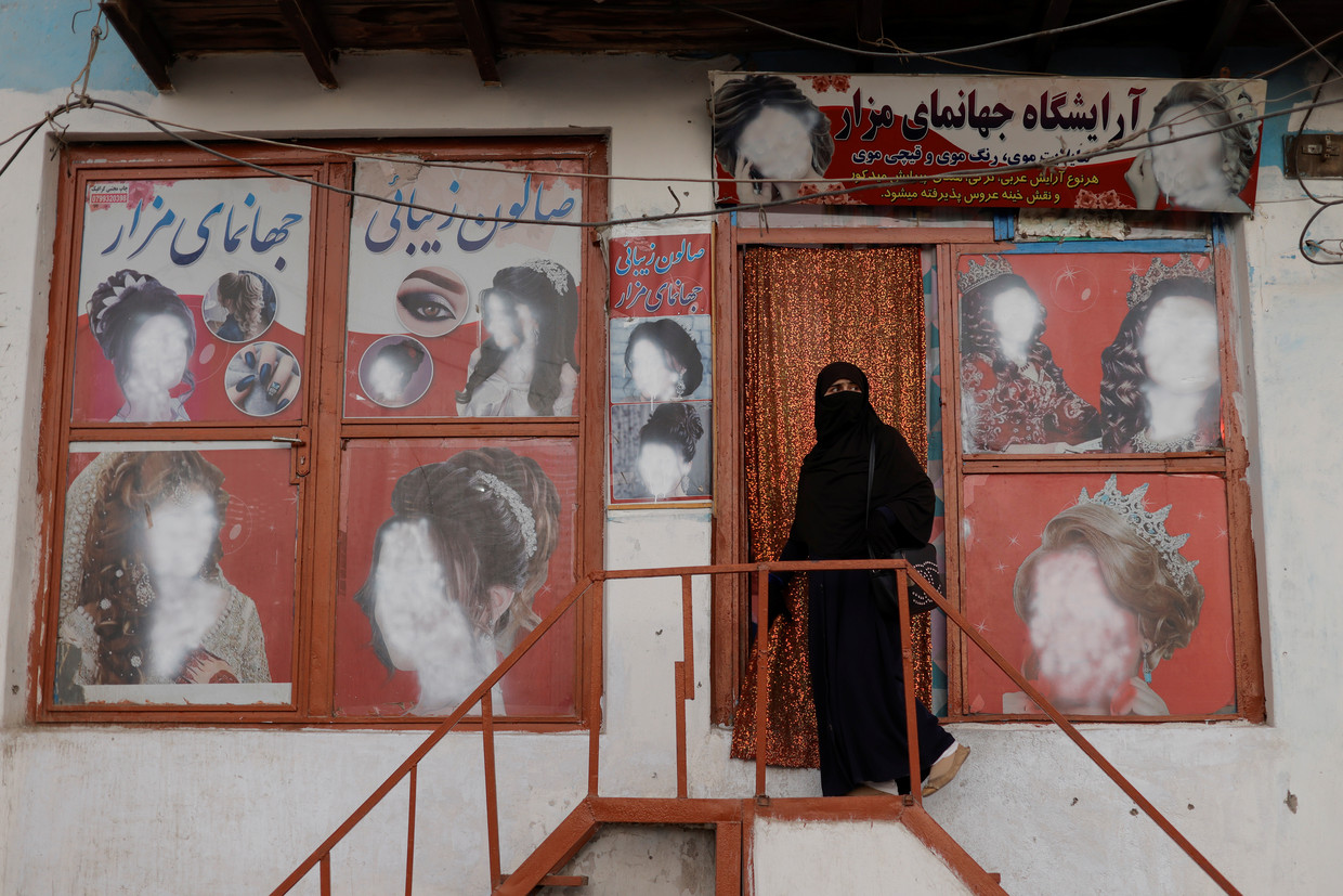 Een vrouw in niqaab gaat in Kaboel een schoonheidssalon binnen waar de gezichten van vrouwen van de afbeeldingen zijn verwijderd. Beeld Reuters
