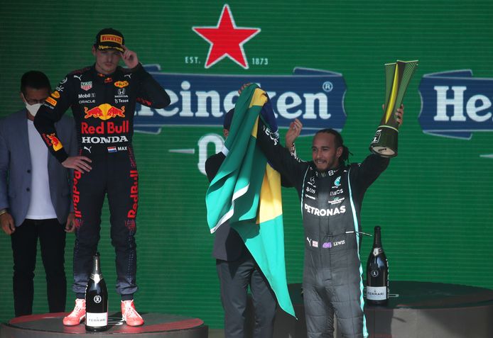 Lewis Hamilton viert zijn zege in Brazilië, terwijl Max Verstappen op de achtergrond toekijkt.