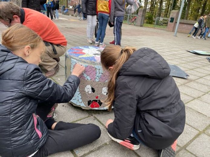 Leerlingen van basisschool De Vendelier in Helmond zijn bezig met het aanbrengen van het mozaïek op een betonnen poef.