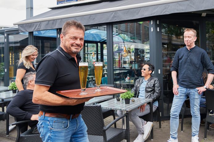 Alex Ulijn serveert een biertje onder het toeziend oog van Jos van Bokhoven (rechts) op het terras van lunchroom Hello. Vanaf 30 mei is Ulijn de nieuwe uitbater.