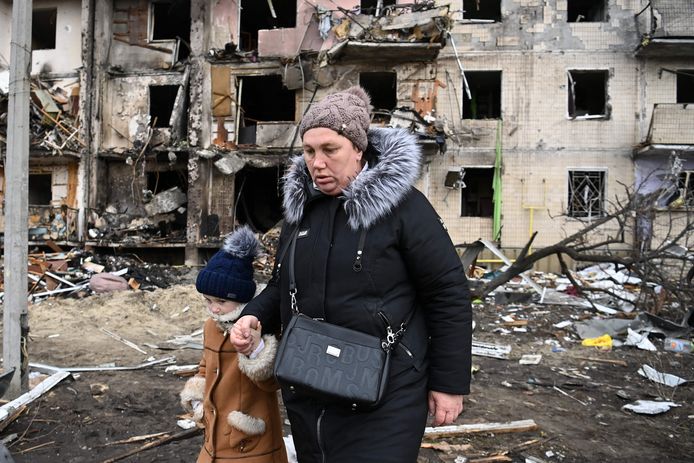 Een vrouw wandelt met haar kind voorbij een gebombardeerd appartementsgebouw in Kiev.
