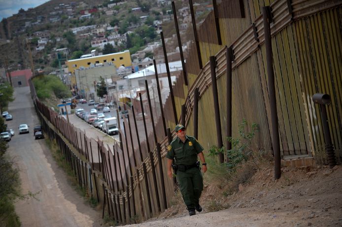 Een Amerikaanse agent inspecteert de grensmuur tussen de VS en Mexico.