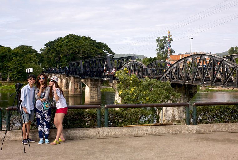 Toeristen maken selfies bij de brug die door krijgsgevangenen gebouwd werd. Beeld  