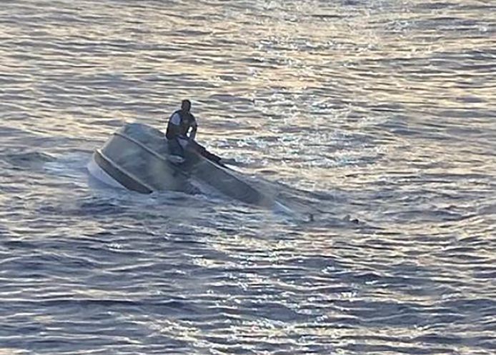 De geredde drenkeling bovenop de ondersteboven maar nog drijvende boot.
