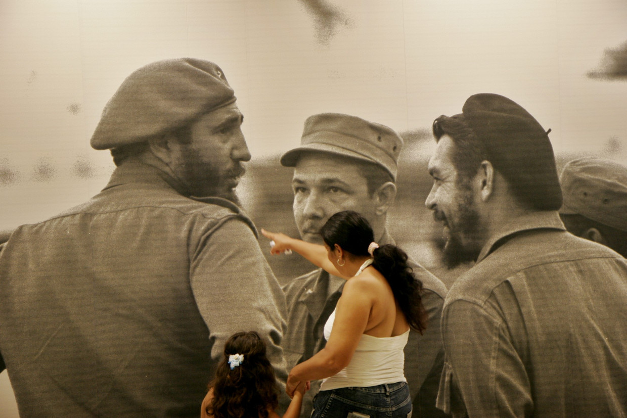 Bezoekers van het Che Guevara-mausoleum in het Cubaanse Santa Clara kijken naar een foto van Fidel en Raúl Castro met Ernesto Che Guevara.  Beeld Getty 