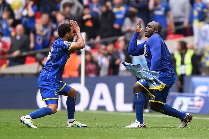 AFC Wimbledon's Adebayo Akinfenwa, right, celebrates scoring his side's second goal of the game from the penalty spot during the their League Two Play-Off Final soccer match against Plymouth Argyle at Wembley Stadium, London, Monday, May 30, 2016. AFC Wimbledon, an English soccer club created in 2002 by disgruntled supporters after their original team was controversially relocated and rebranded, continued its rise up the league pyramid by getting promoted to the third tier on Monday. The south London team beat Plymouth 2-0 in the fourth-tier League Two playoff final at Wembley Stadium. (Andrew Matthews/PA via AP)      UNITED KINGDOM OUT   NO SALES   NO ARCHIVES