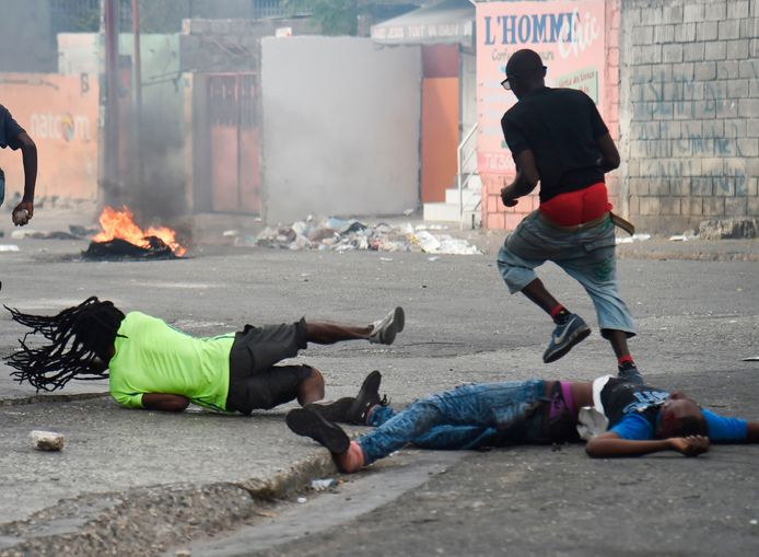 Een man valt terwijl hij het lichaam van een dode kameraad mee wil slepen in Port-au-Prince.