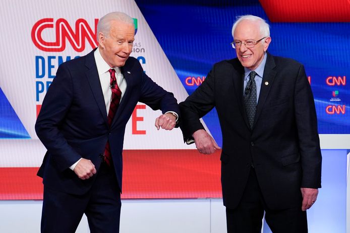 Joe Biden en Bernie Sanders begroeten mekaar met een elleboog tijdens hun rechtstreekse debat.