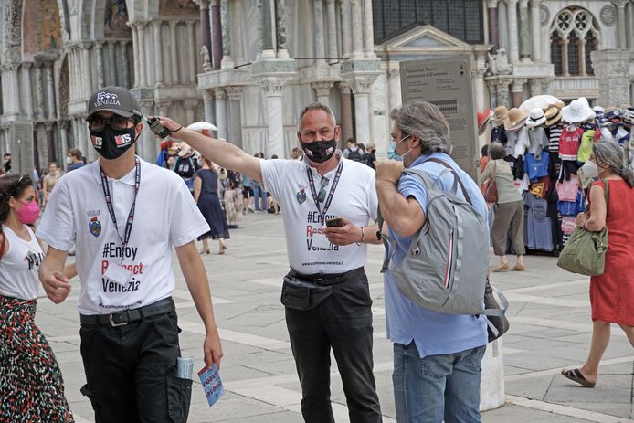 Corona-stewards wijzen toeristen de weg aan het San Marco-plein in Venetië.