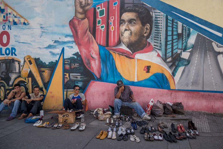 Schoenverkopers in de straten van Caracas, voor een muurschildering van president Nicolás Maduro.  Beeld EPA