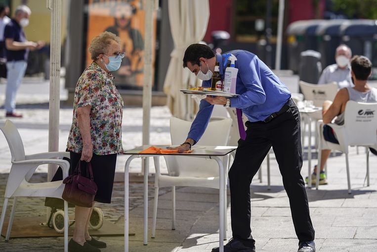 Een ober maakt een tafeltje schoon aan een plein in Madrid.  Beeld Bloomberg via Getty Images