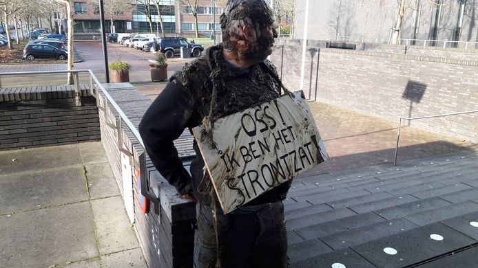 Arie den Dekker heeft zich met koeienstront bedekt en vastgeketend aan een trapleuning voor het Osse gemeentehuis.