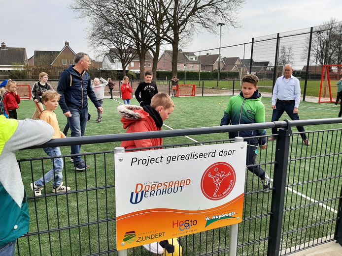 Wethouder Twan Zopfi en Cees Oostvogels (rechts) nemen met een partijtje voetbal met kinderen van de Sint Jozefschool feestelijk de nieuwe voetbalkooi bij VV Wernhout in gebruik