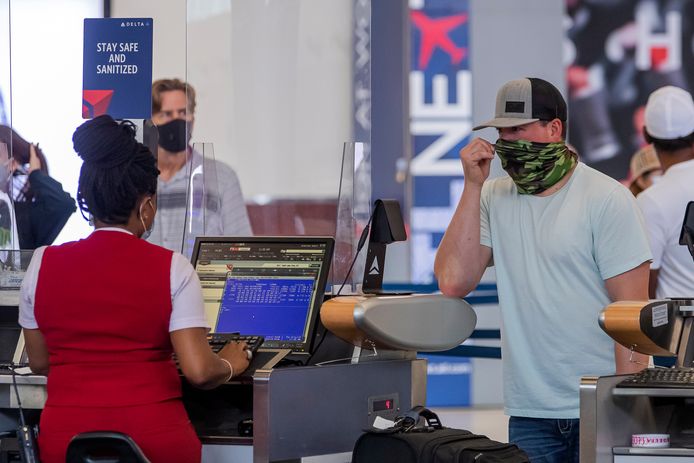 Mensen met mondkapjes en sjaals op bij een desk van Delta Airlines op een luchthaven in de VS.