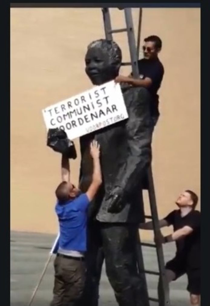 Op het filmpje is te zien hoe drie mannen met behulp van een ladder het standbeeld  van Nelson Mandela in Scheveningen voorzien van een bord.