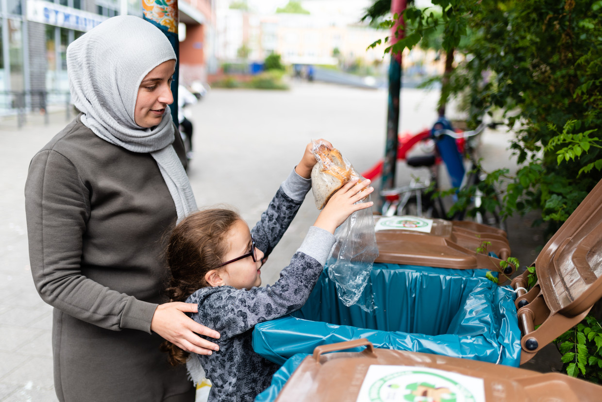 Moeder en kind legen een zak oud brood in een van de broodbakken op het Oleanderplein in Rotterdam. Beeld Katja Poelwijk
