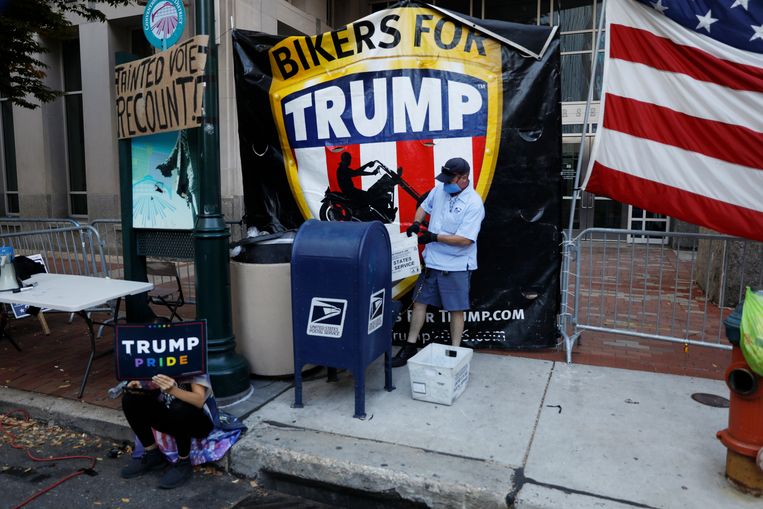 Een medewerker van het postbedrijf leegt een brievenbus omgeven door pro-Trump protestborden. Beeld AP